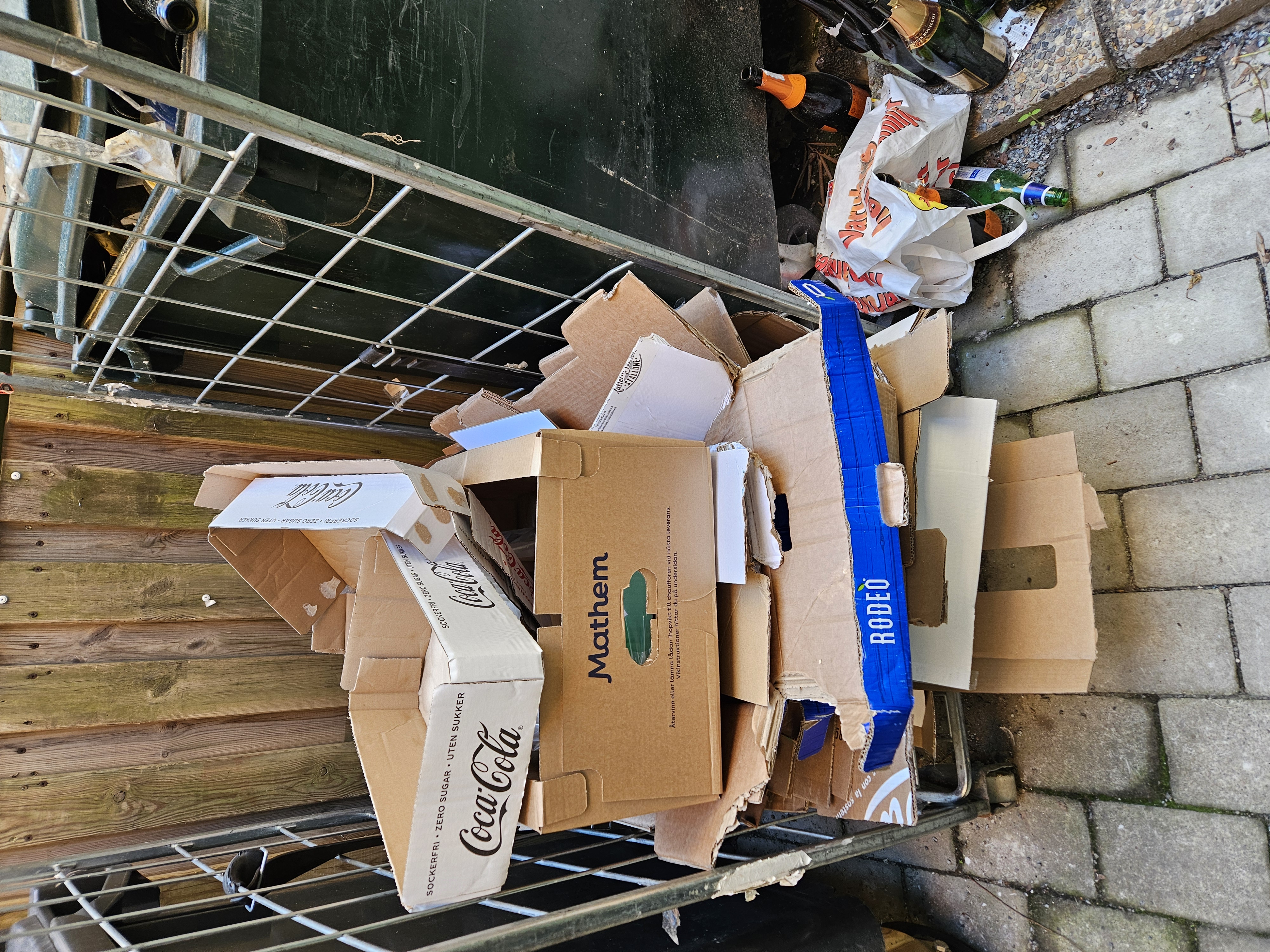 Cartons déchirés, bouteilles vides et déchets au sol derrière un restaurant